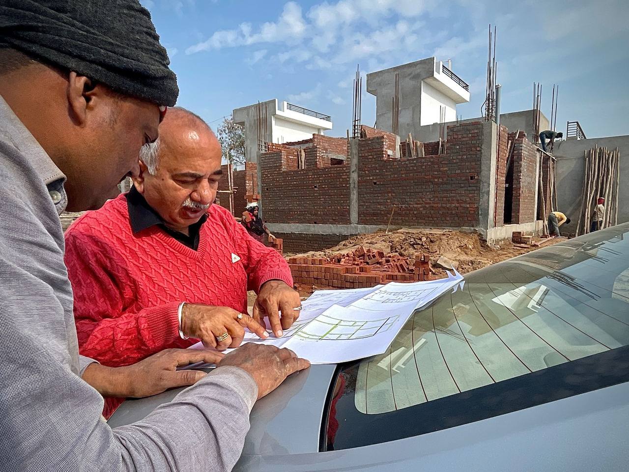 Two people reviewing site plans on a car hood at a construction site