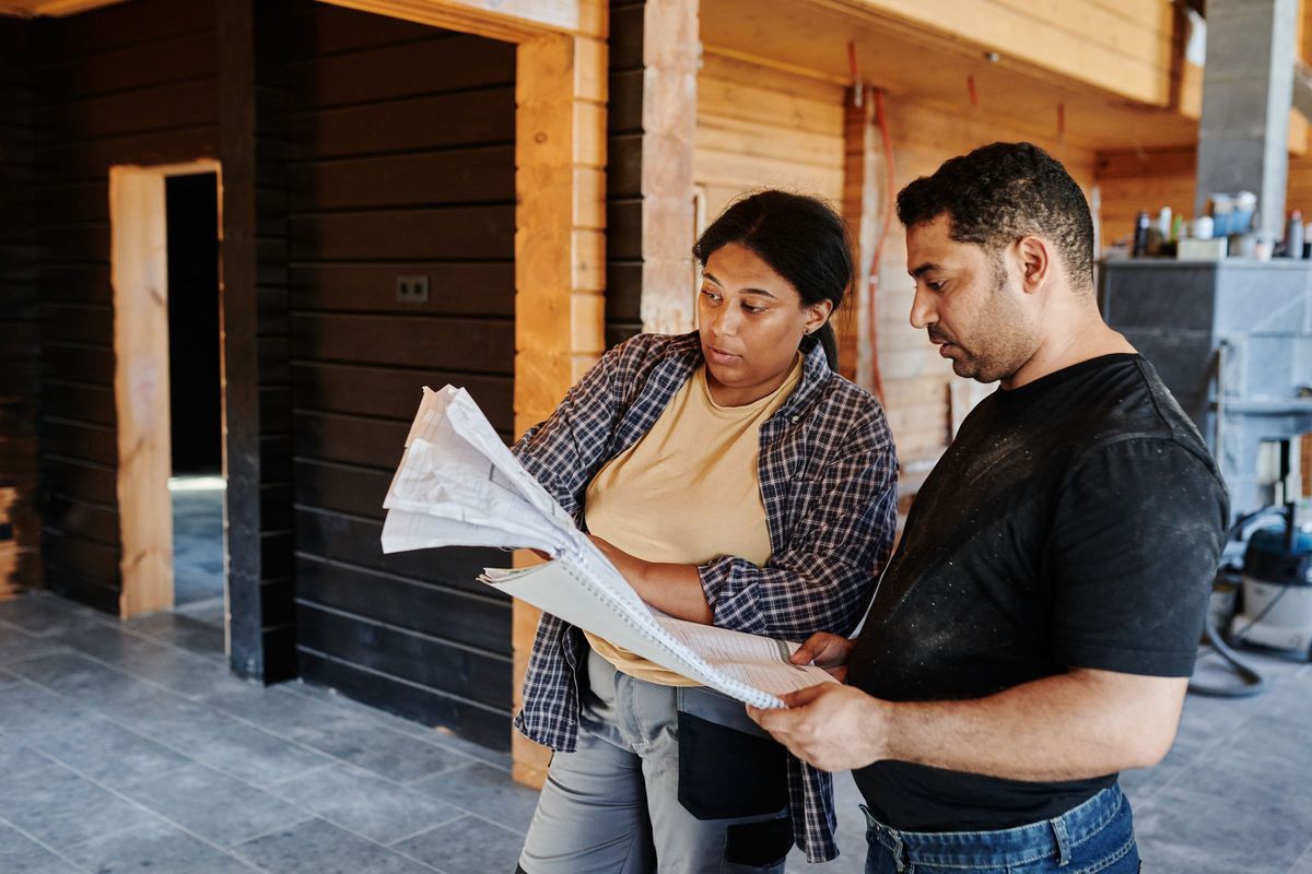 Two people reviewing building plans inside a house under construction